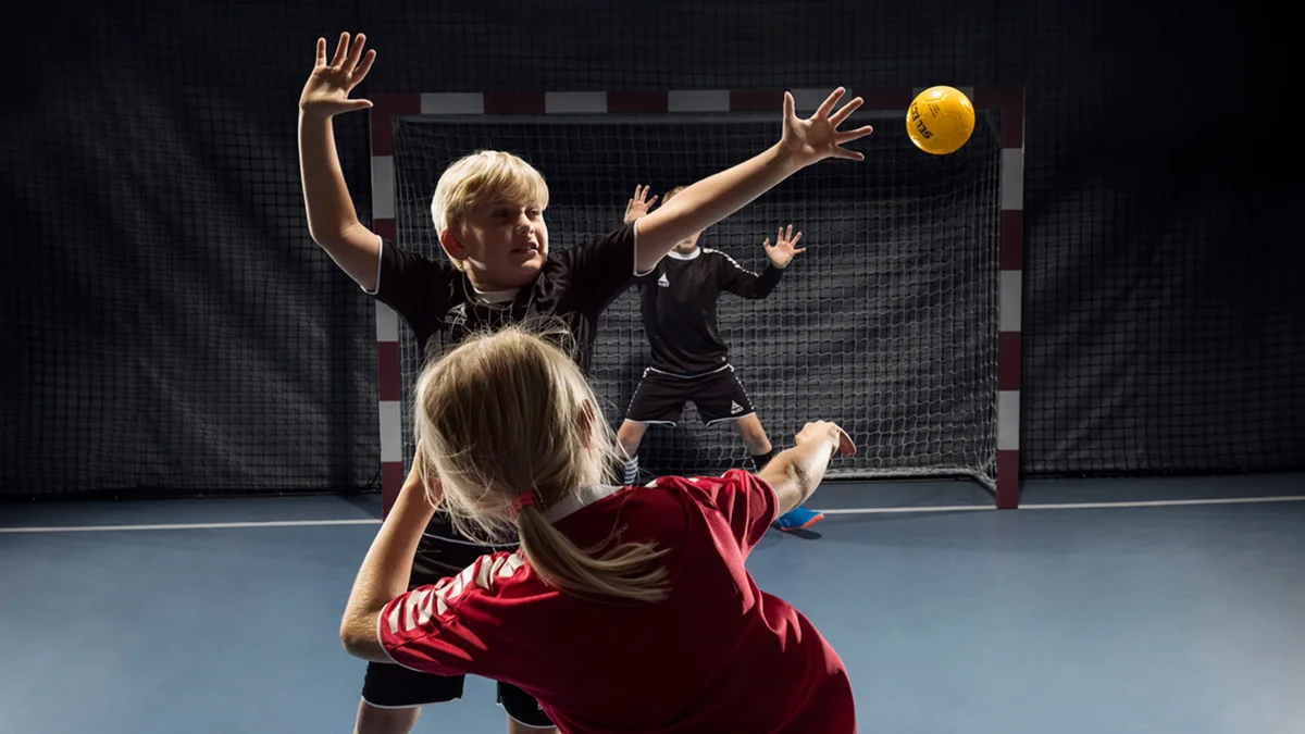 Barn som spiller håndball i hall, med fokus på teknikk og spillsituasjon foran mål
